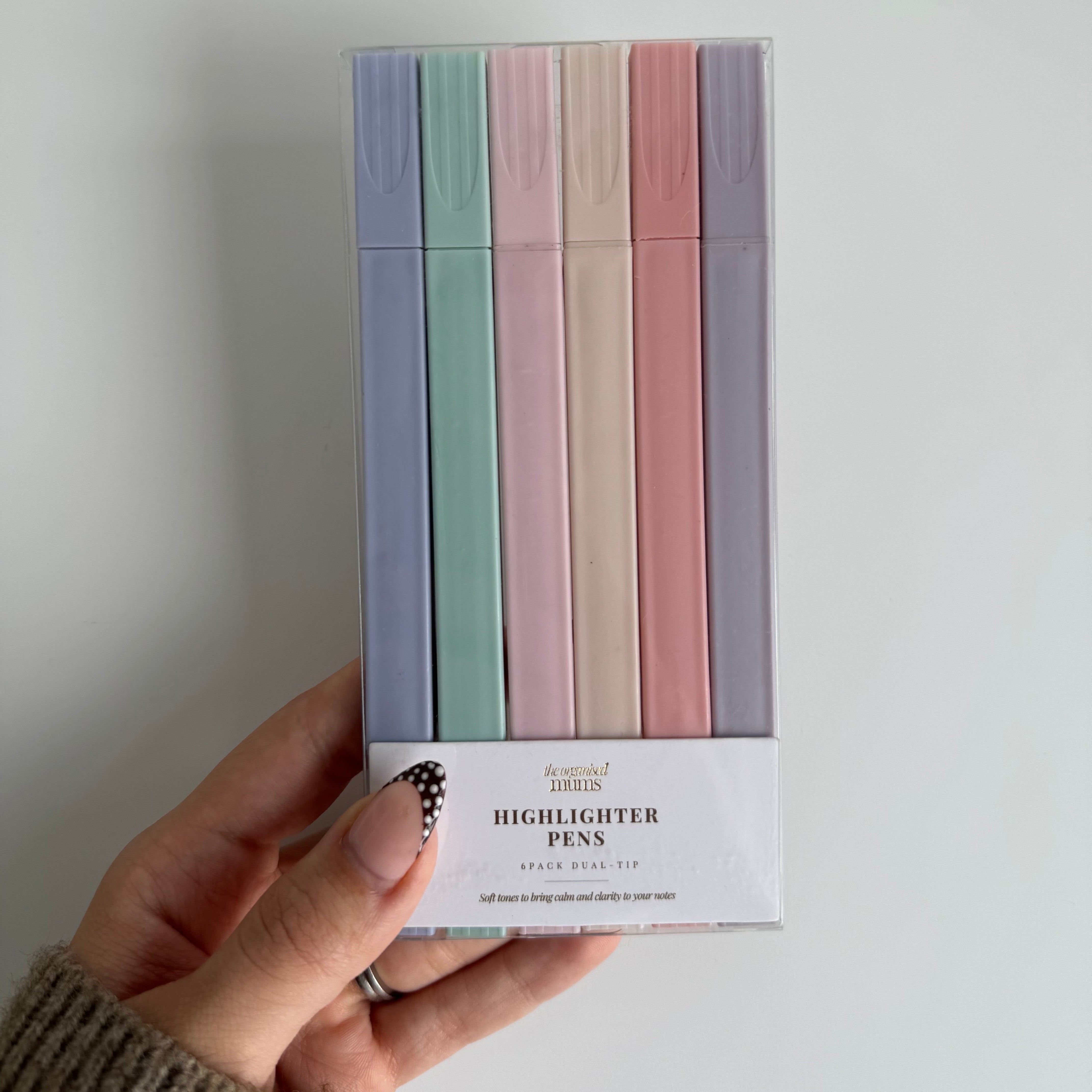 Hand holding a box of pastel-colored highlighter pens against a white background